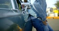 Close-up of a woman in a denim jacket and jeans leaning on a classic car, she puts her hand in her pocket