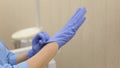 Close-up of a woman dentist`s hand putting on blue sterilized surgical gloves.