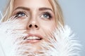 Close up Woman Face Portrait with White Feather. Blond Model with Blue Eyes Long Lashes and White Teeth covering Cheeks