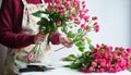 Close-up of a woman florist`s hand in a flower apron making a bouquet of pink roses in a flower shop at work. The concept of the