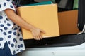 Close up on woman hand holding and carrying a cardboard box with stuffs moving into the car to relocation on moving day.