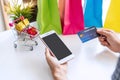 Close up of woman hand holding credit card while using smartphone with miniature gift boxes in trolley and colorful bags on white Royalty Free Stock Photo