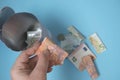 Close-up woman hand holding 10-euro folded bill over blurred open piggy bank,pile of money,banknotes,coins poured out