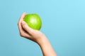 Close up woman hand holding green apple against blue background. choosing healthy lifestyle Royalty Free Stock Photo