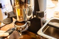 Close up woman hand holding portafilter, girl barista is grinding the roasted coffee beans into powder using coffee grinder at Royalty Free Stock Photo