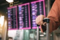 Close up of woman hand holding suitcase standing at the airport checking arrival departure board with the flight schedule in Royalty Free Stock Photo