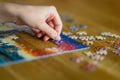 Close-up on woman hand playing puzzles at home. Connecting jigsaw puzzle pieces in a living room table, assembling a jigsaw puzzle