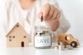 Close up of woman hand putting coin into glass jar for saving money, stack of coins, toy house and car on table, saving money and Royalty Free Stock Photo