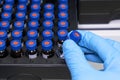 Close up woman hand in a rubber gloves put sample in a glass vial with blue cap into the autosampler rack in HPLC system