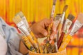 Close up of woman hand touching a wooden flask with paint brushes in a blurred background