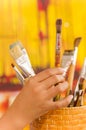 Close up of woman hand touching a wooden flask with paint brushes in a blurred background