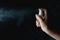 Woman handing small spray bottle and spraying on dark background