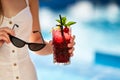 Close-up of woman hands with cocktail glass and sunglasses. Female holding a drink and sun shades near swimming pool Royalty Free Stock Photo