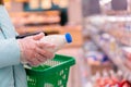 Close up of woman hands in gloves holding a shopping basket and choosing milk in a supermarket. Shopping during Royalty Free Stock Photo