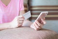 Close up woman hands holding credit card and using cell phone for online shopping on sofa in the living room of the house. Royalty Free Stock Photo