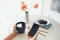 Close up of woman hands holding cup of tea and mobile phone, reading news, social network, surfing the web in while staying at Royalty Free Stock Photo