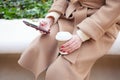 Close up of woman hands with red nails manicure holding cell phone, using internet while sitting on the bench and drinking take Royalty Free Stock Photo