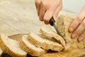 Close up of woman hands slicing a loaf of homemade bread with sesame seeds on a wooden cutting board in selective focus on wooden Royalty Free Stock Photo