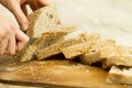Close up of woman hands slicing a loaf of homemade bread with sesame seeds on a wooden cutting board in selective focus on wooden Royalty Free Stock Photo