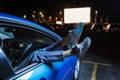 Close up of woman hanging her legs out of car window while watching a movie at drive in cinema from the front seat of Royalty Free Stock Photo