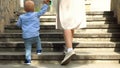 Close up of woman helping her little child boy to climb the stairs by holding his hand. Stock footage. Mother with small Royalty Free Stock Photo