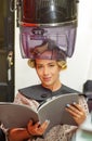 Close up of woman holding a book in her hands and waiting under an old hair-dryer chair hood, in a blurred background Royalty Free Stock Photo