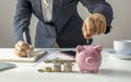 Close-up of a woman holding a coin in a pig piggy bank.