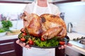 Close-up woman holding garnished roasted turkey on a kitchen background. Thanksgiving turkey concept.