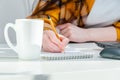 Close-up woman holding pencil in hand writing in notepad on workplace with coffee cup and laptop. Woman working at home Royalty Free Stock Photo