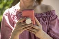 Close-up of woman holding and reading from a cell phone in pink case with grip handle on back - off shoulder blouse and short