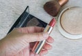 Woman holds lipstick in nude color in left hand for make-up with powder with brush backdrop Royalty Free Stock Photo