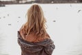 Close-up of woman with long wavy fair hair wearing brown sweatshirt, woolen cardigan, standing on sandy beach of river. Royalty Free Stock Photo