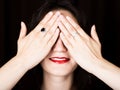 Close-up woman looks straight into the camera on a black background. laughing woman covering her eyes with her hand