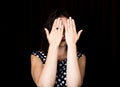 Close-up woman looks straight into the camera on a black background. laughing woman covering her eyes with her hand