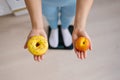 Close-up of a woman making a choice between a peach fruit and a donut on the background of scales. Diet concept Royalty Free Stock Photo