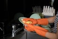 Close up woman protective gloves washing dishes with sponge in the kitchen sink Royalty Free Stock Photo