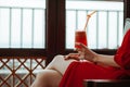 Close up of woman in red dress with red cocktail with orange straw in hands. Beautiful girl in red dress drinking