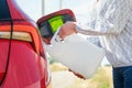 Close up woman refilling the red car with fuel or a diesel engine fluid from canister in the field. Royalty Free Stock Photo