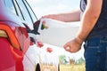 Close up woman refilling the red car with fuel or a diesel engine fluid from canister in the field. Royalty Free Stock Photo