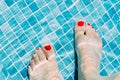 Close up of woman`s feet with red nail polish in a pool with blue tiles