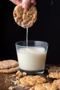 Close-up of woman`s hand with chocolate chip cookie, falling milk into a glass, on table with cookies and crumbs Royalty Free Stock Photo