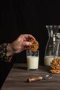 close-up of woman`s hand with chocolate cookie in hand over glass of milk, on a table with milk bottle and cookies, black backgro Royalty Free Stock Photo