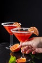 Close-up of woman`s hand holding a glass of blood orange cocktail, with another in the background out of focus, on a black backgr Royalty Free Stock Photo