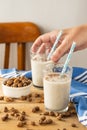 Close-up of a woman`s hand holding a glass of horchata with a straw, on a table with tiger nuts and a blue cloth, white backgroun Royalty Free Stock Photo