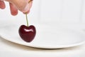 Close-up of a woman& x27;s hand holding a heart-shaped cherry on a white plate. Ripe fresh juicy berry on a white