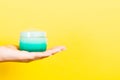 Close up of woman`s hand holding a jar of cosmetics product at yellow background with copy space Royalty Free Stock Photo