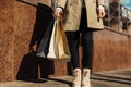 Close-up of woman`s hand holding shopping bags on the street, woman in beige raincoat and autumn shoes Royalty Free Stock Photo