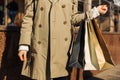 Close-up of woman`s hand holding shopping bags on the street, woman in beige raincoat and autumn shoes Royalty Free Stock Photo