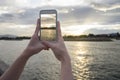 Close up of woman's hand holding smart phone, mobile, smart phone over blurred beautiful sea with sunset moment to take a pho