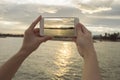 Close up of woman's hand holding smart phone, mobile, smart phone over blurred beautiful sea with sunset to take a photo
